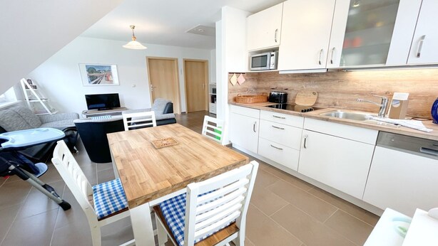 A modern kitchen with white cabinets, a wooden dining table, and a microwave.