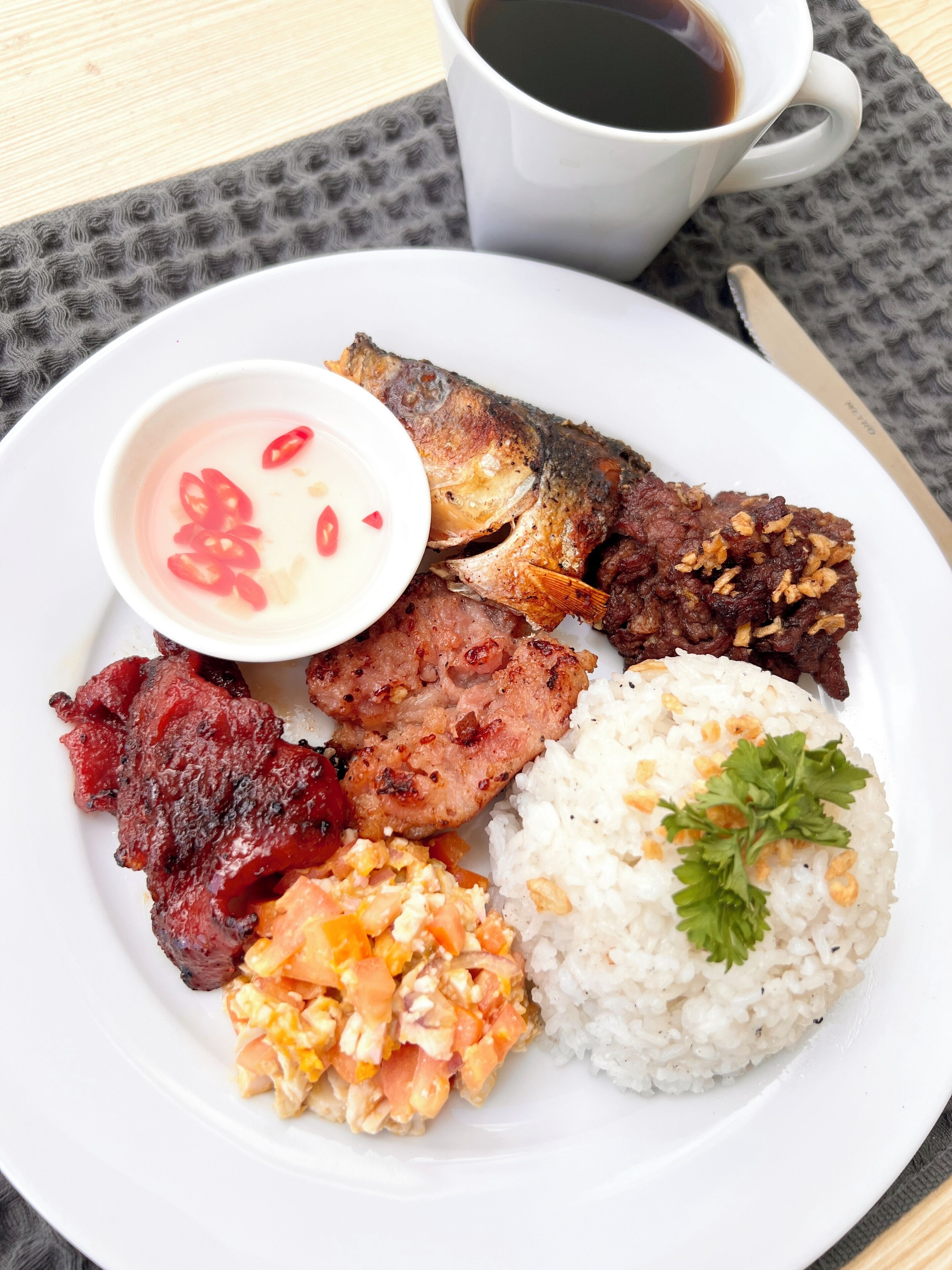 A plate with fried fish, meat, rice, and a small bowl of sauce.