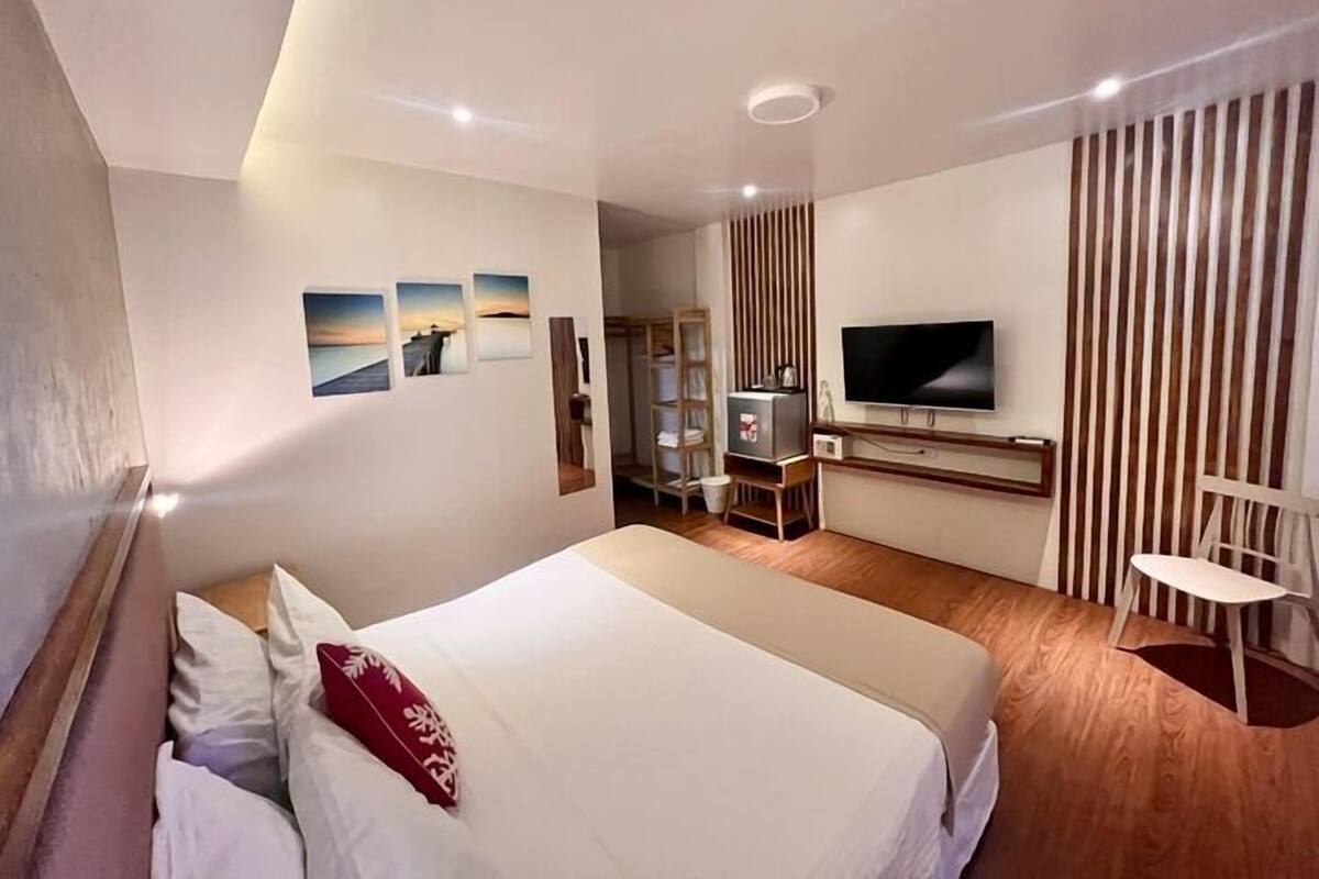 Ein modernes Hotelzimmer mit einem großen Bett, einem Fernseher, einem Schreibtisch und einem Sessel.