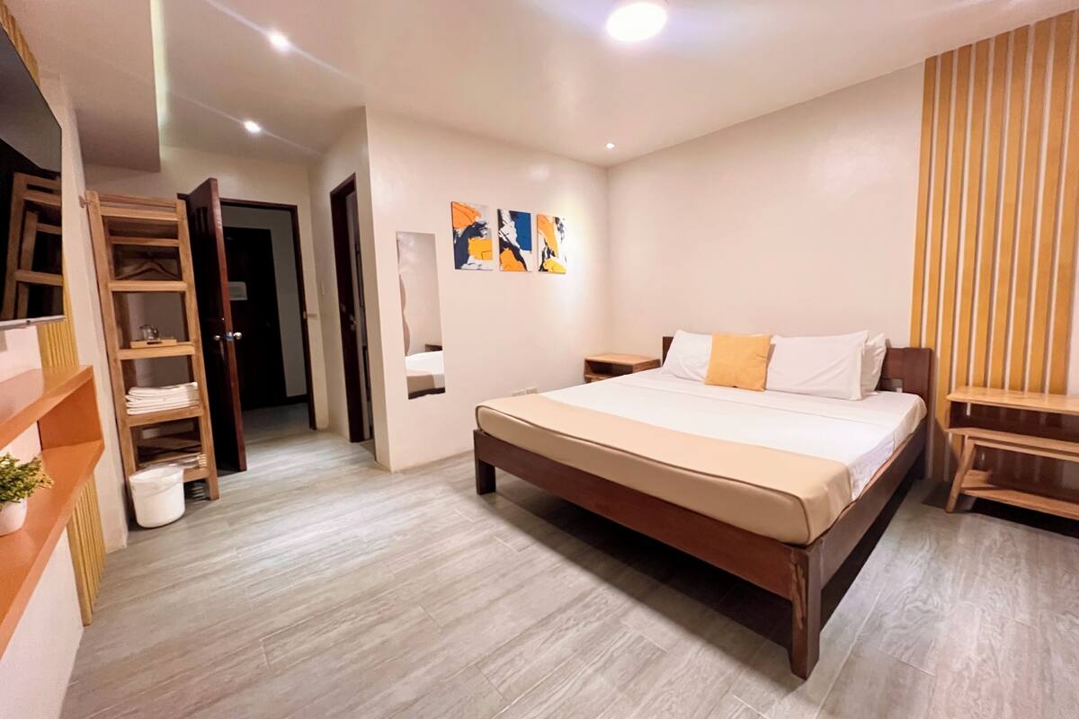 Ein modernes Schlafzimmer mit einem großen Bett, einem Holzschrank, einem kleinen Nachttisch und abstrakter Wandkunst.