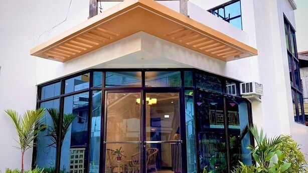 A corner building with a glass facade, wooden overhang, and indoor seating area visible through the glass. - La Palme (El Nido)