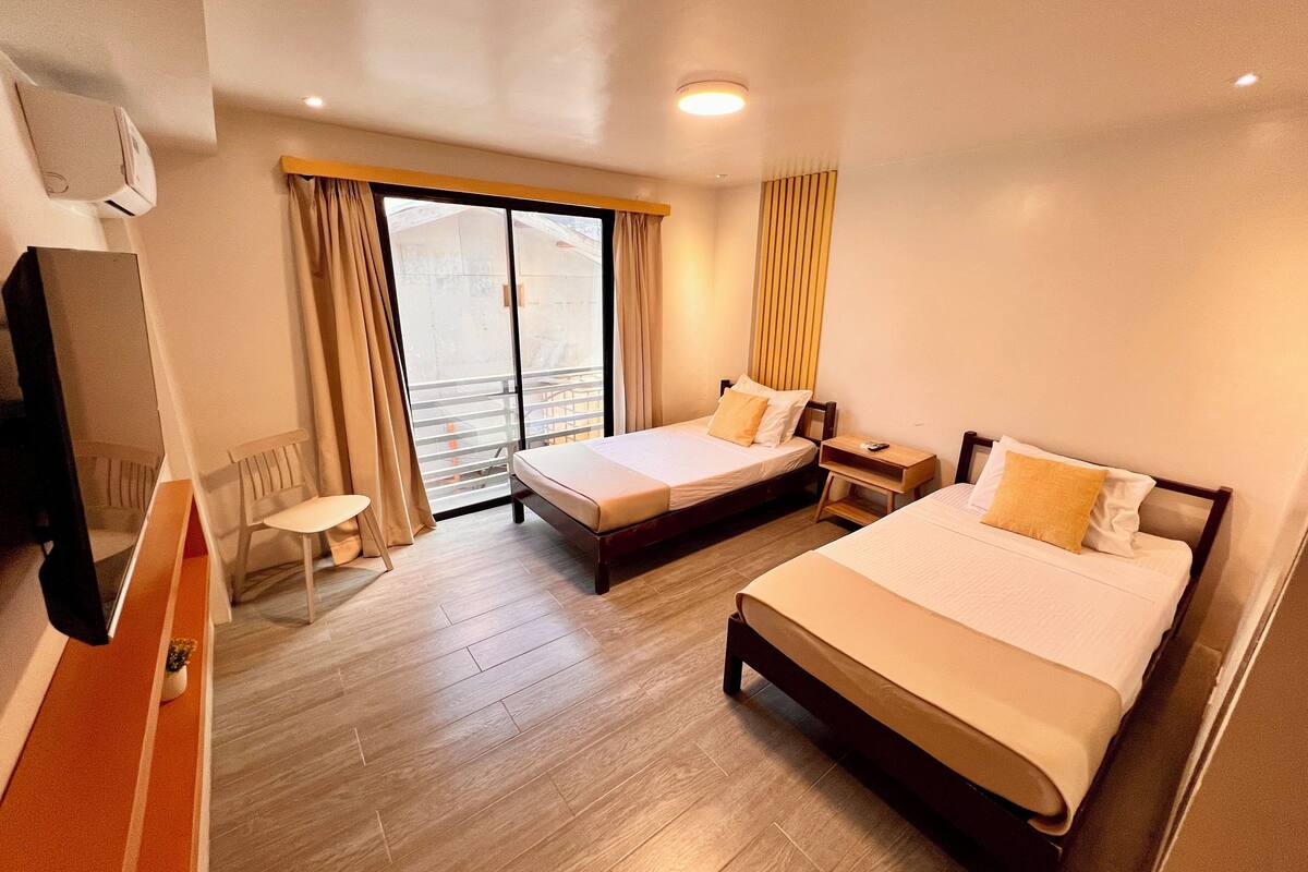 Ein Hotelzimmer mit zwei Betten, einem Schreibtisch, einem Stuhl und einem großen Fenster mit Vorhängen.