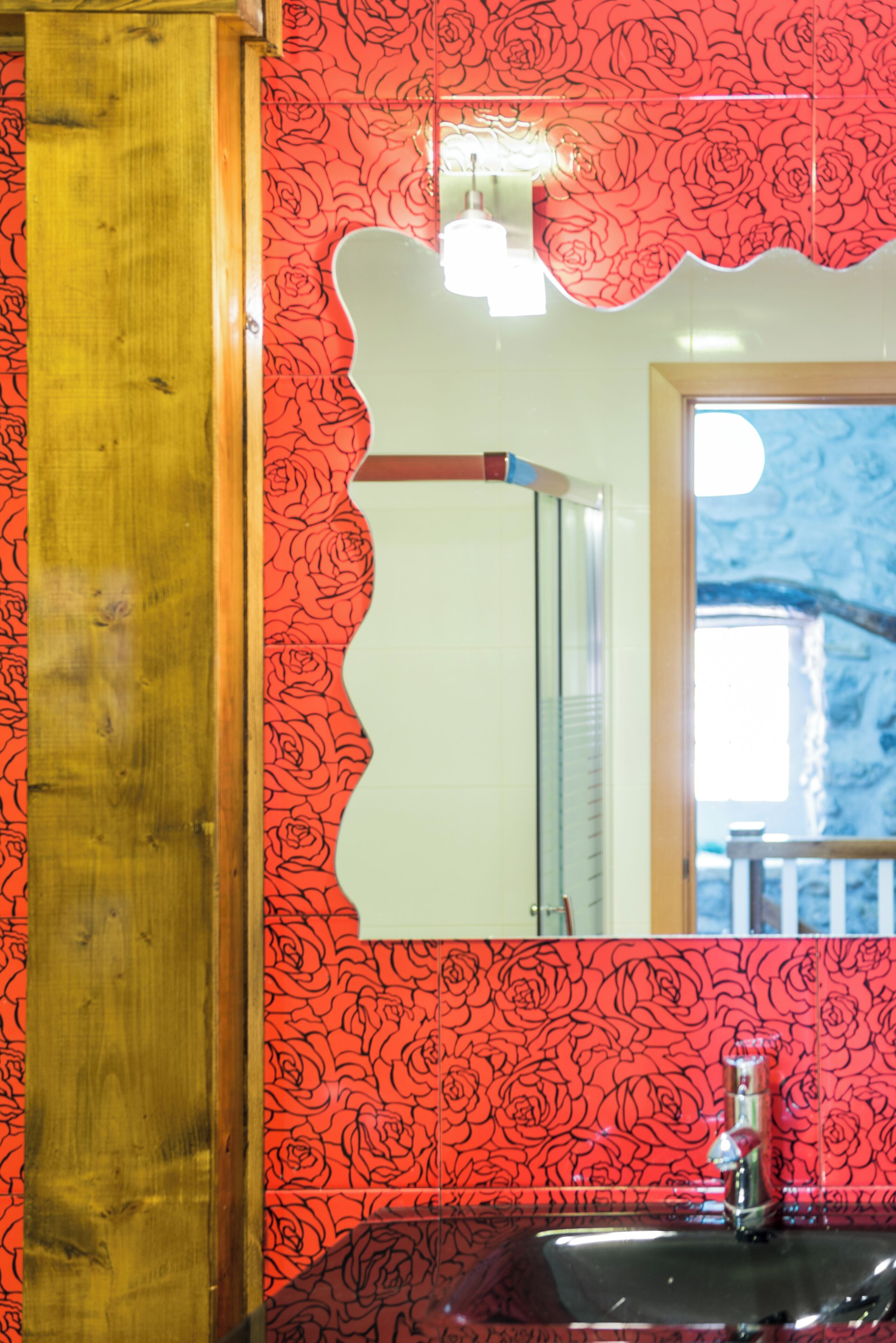 A bathroom with a wooden vanity, a sink, and a mirror with a red floral pattern.
