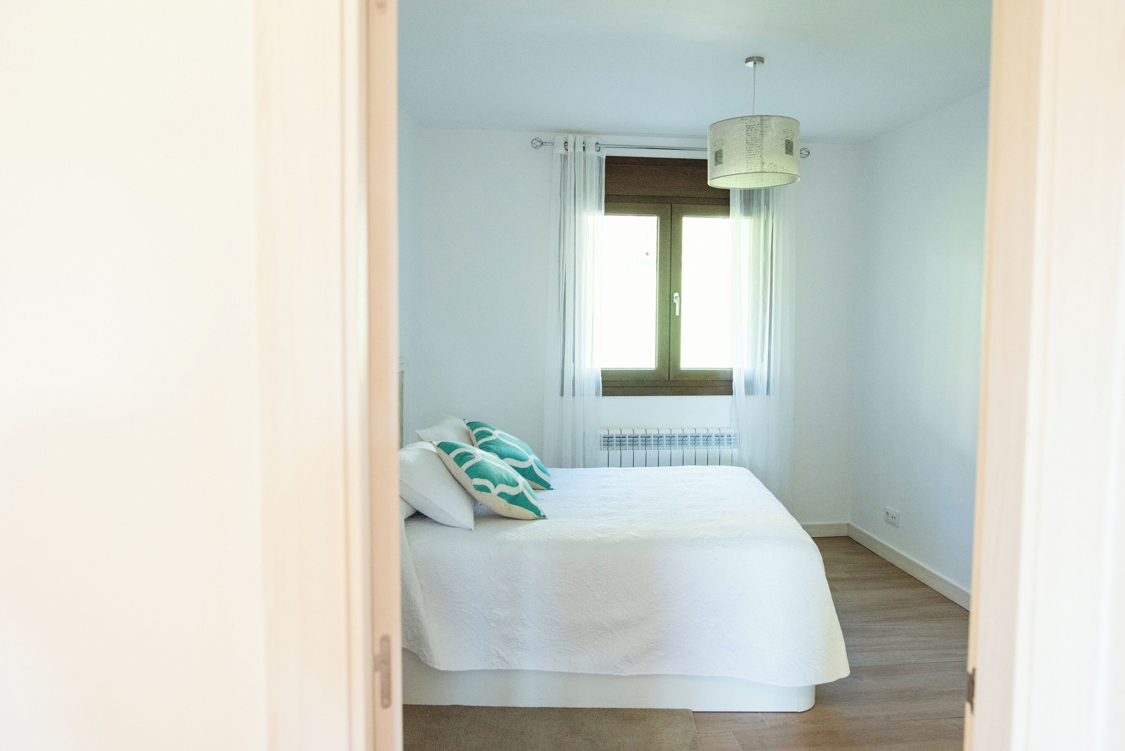 Een slaapkamer met een bed, een raam met gordijnen, een radiator en een plafondlamp.