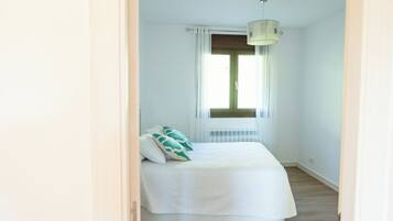Een slaapkamer met een bed, een raam met gordijnen, een radiator en een plafondlamp.