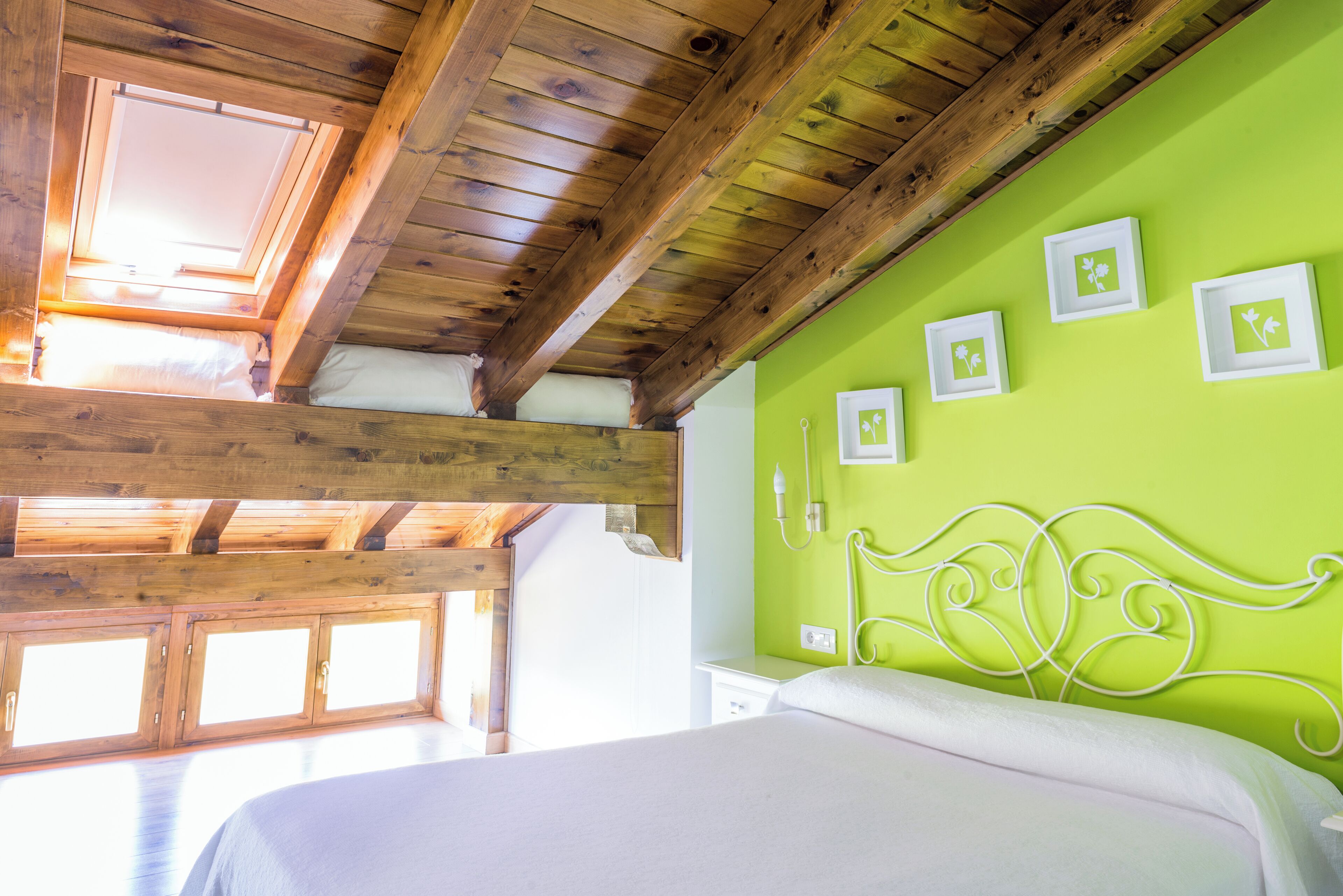 A bedroom with a wooden ceiling, a green wall, and a bed with a white headboard.