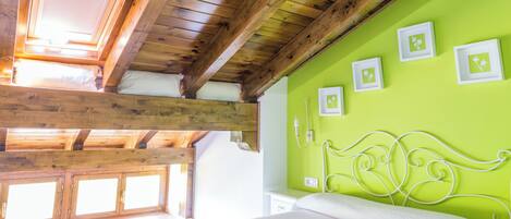 A bedroom with a wooden ceiling, a green wall, and a bed with a white headboard.