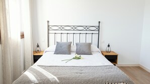 Un lit bien fait, recouvert d’une couvre-lit à motifs, avec deux oreillers et une seule fleur. Il y a deux tables de chevet avec des lampes.