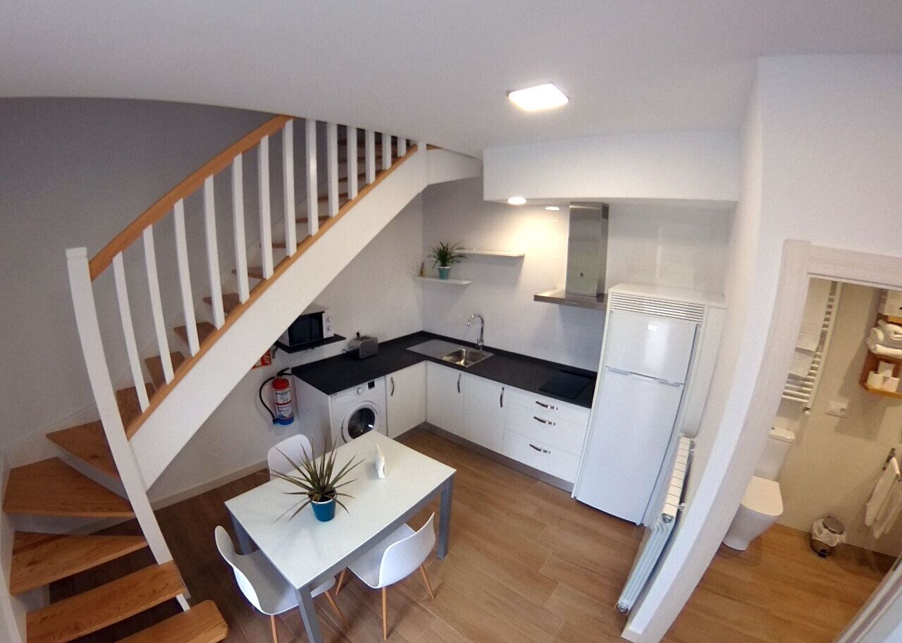 A compact kitchen with a wooden staircase, white cabinetry, and a dining area with a table and chairs.