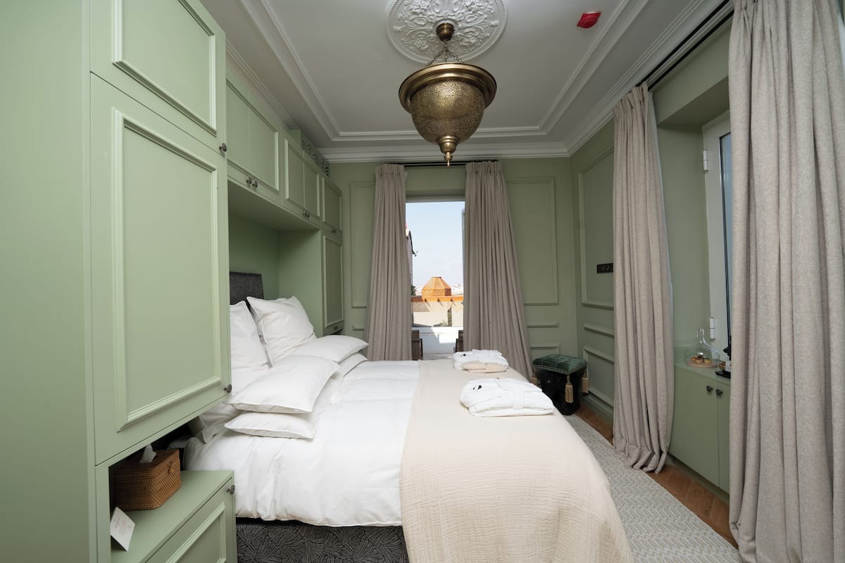 A neatly arranged bedroom with a bed, bedside tables, a hanging light fixture, and a view through a window.