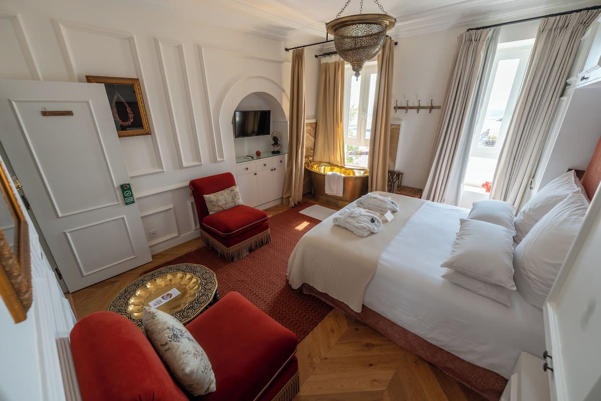 A hotel room with a large bed, a red sofa, a small table with a tray, a television, and a window with curtains.