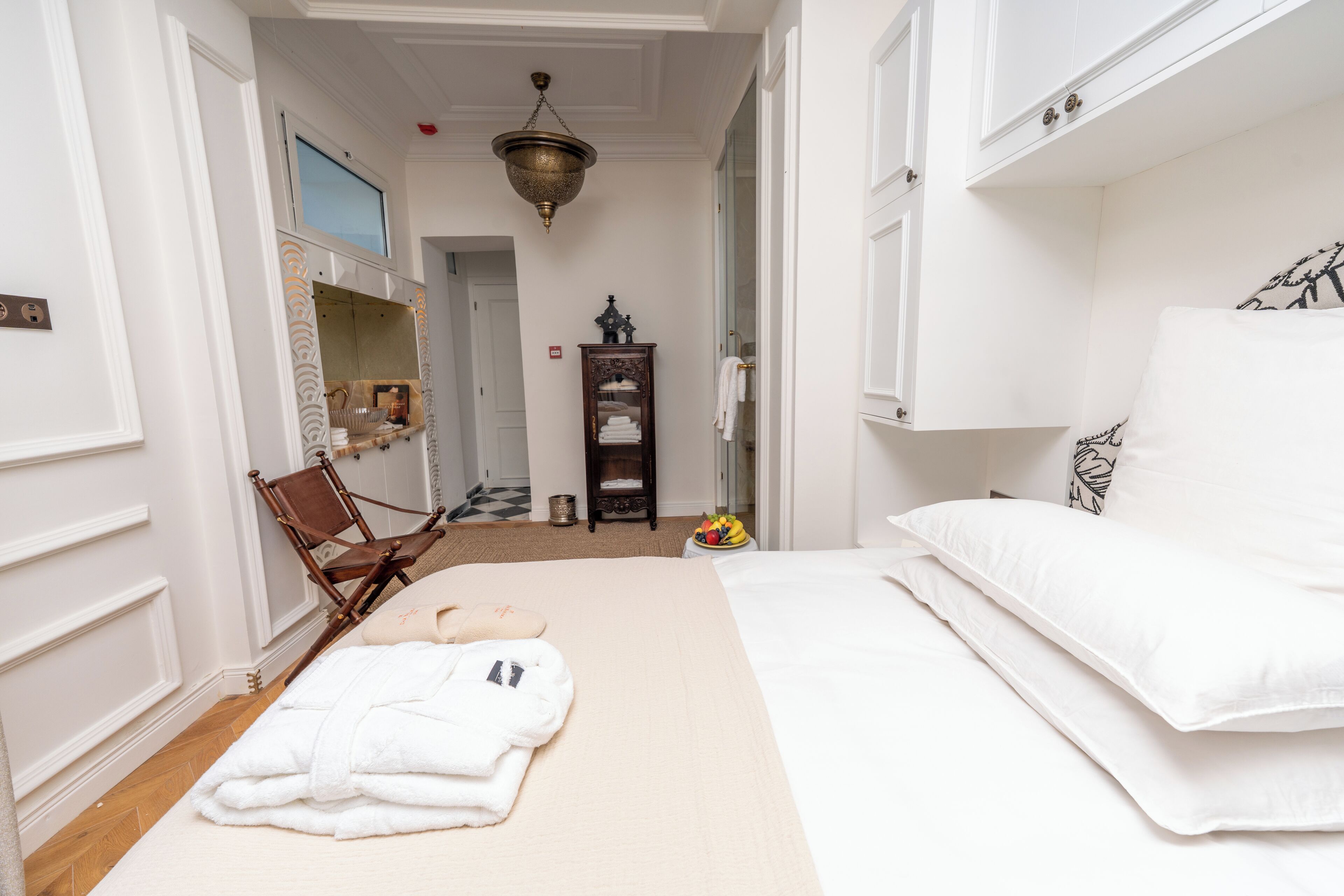 Ein Hotelzimmer mit einem Bett, einem Sessel, einem Bademantel und einem kleinen Tisch mit einer Obstschale.