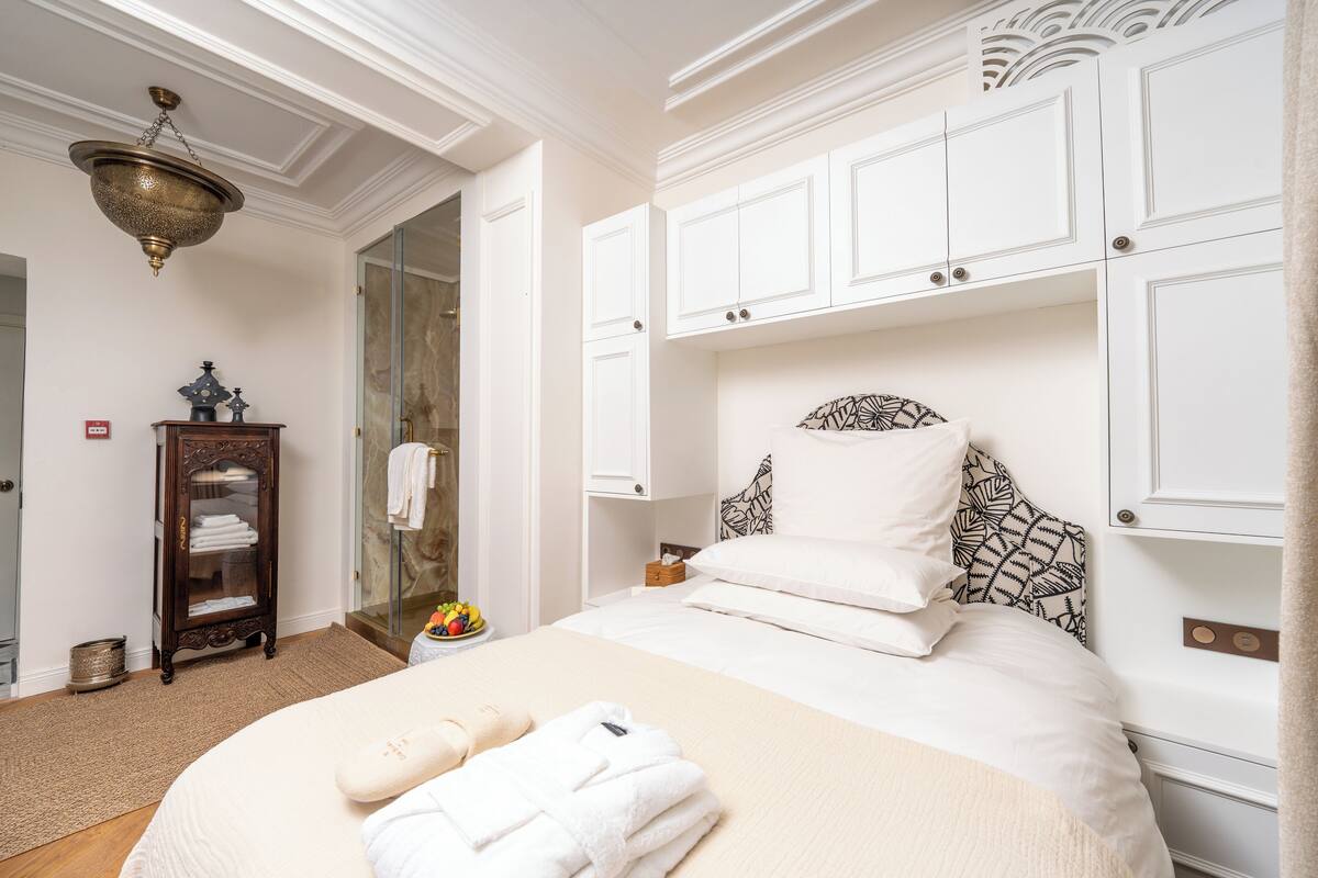 A hotel room with a bed, white cabinets, a wooden cabinet, and a glass shower area.