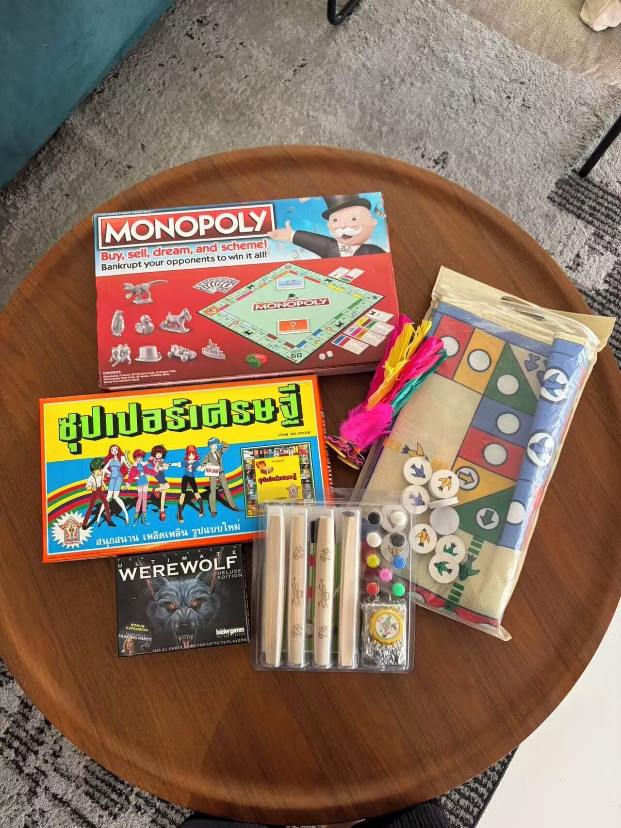 Ein Monopol-Brettspiel, ein farbenfrohes Brettspiel und ein Werwolf-Kartenspiel auf einer Holztischplatte.