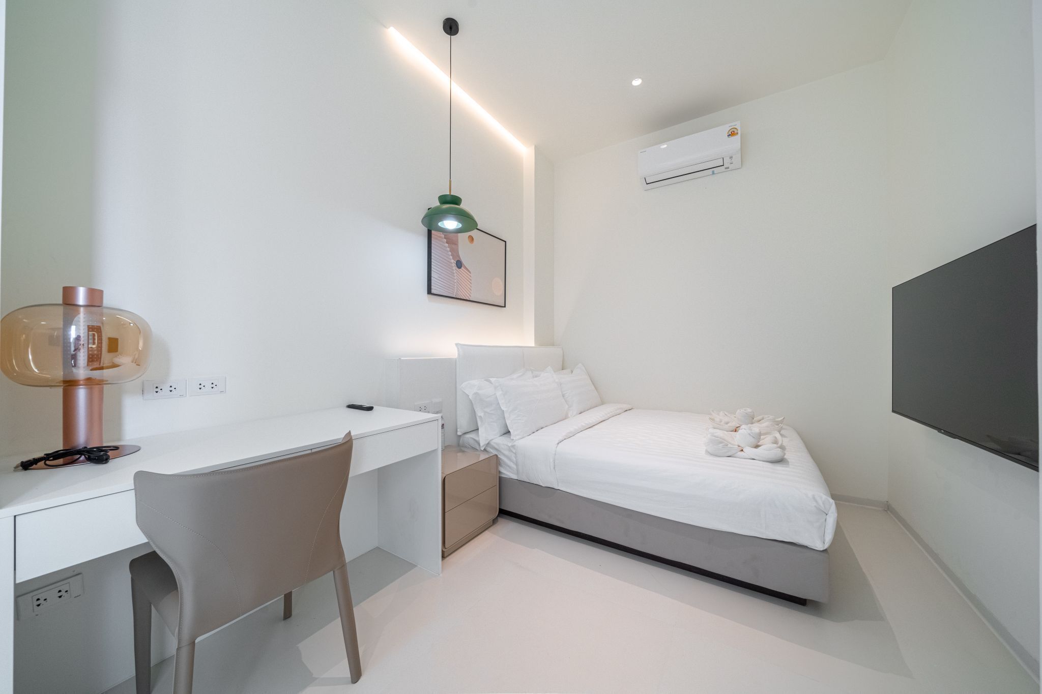 A modern bedroom with a bed, desk, chair, and a wall-mounted air conditioner.