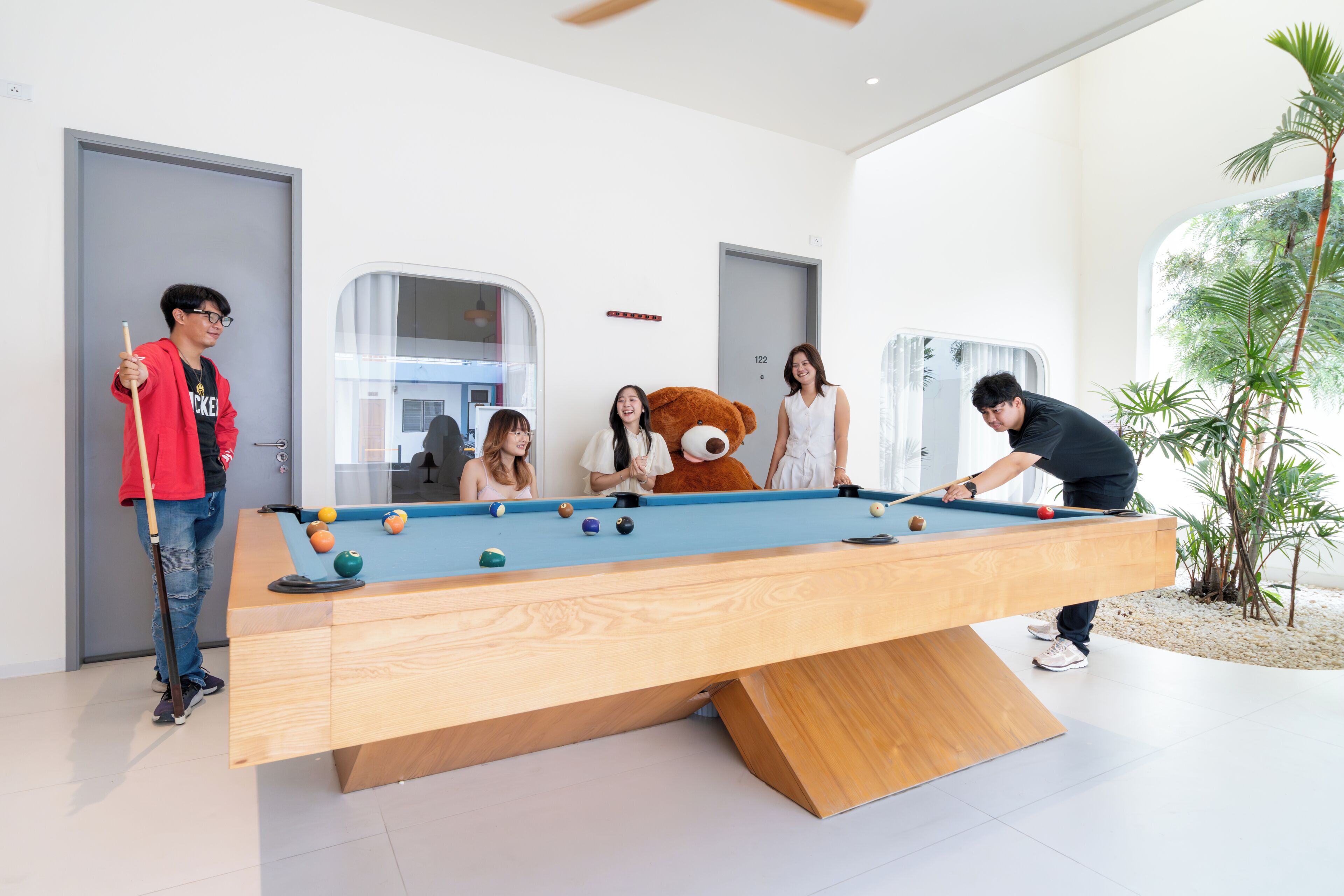 Una mesa de billar en un ambiente interior moderno, con una gran decoración de oso de peluche.