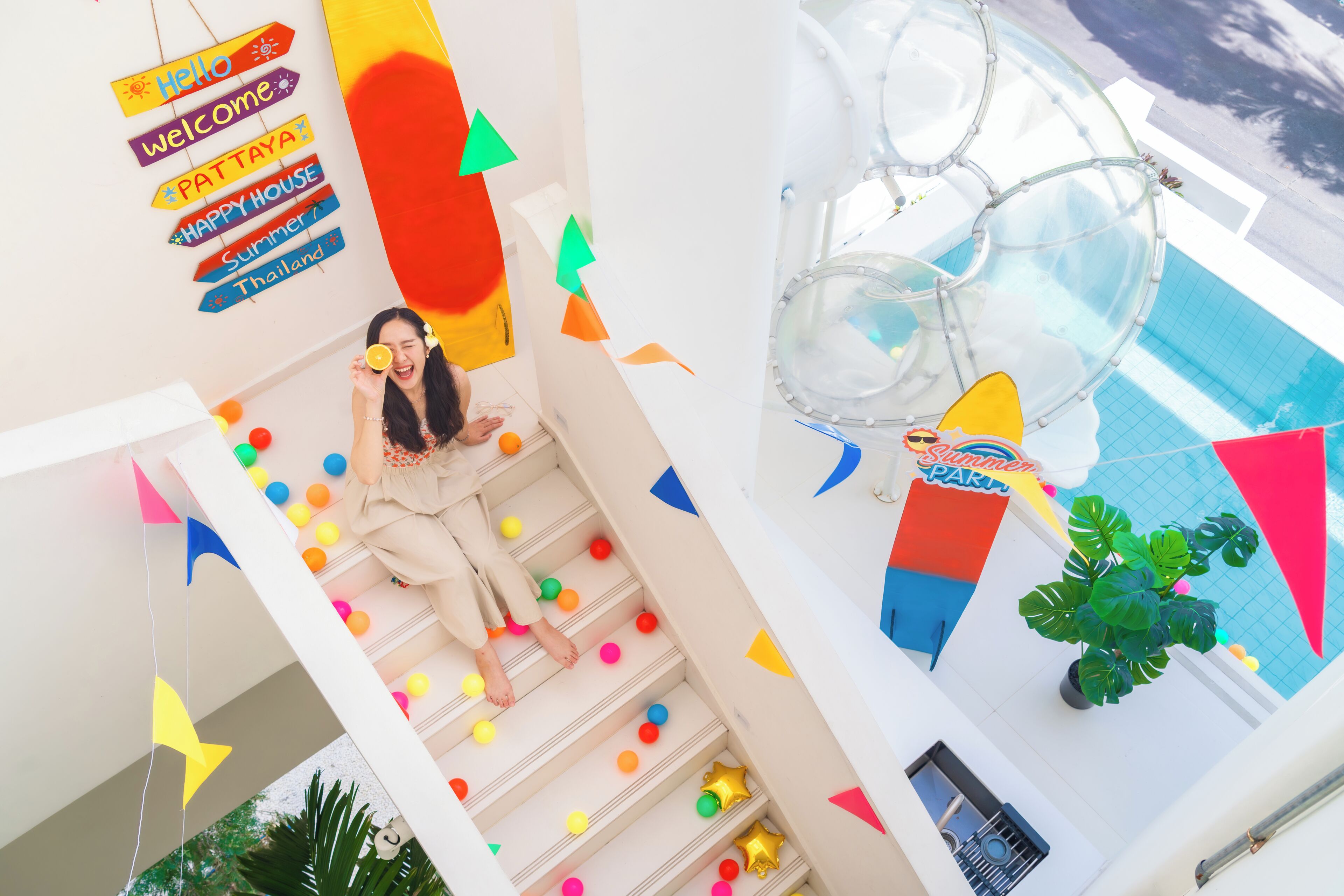 Eine Person auf einer Treppe mit farbenfroher Dekoration und einem Schild mit der Aufschrift 'Welcome to Pat Taya Summer House Thailand'.