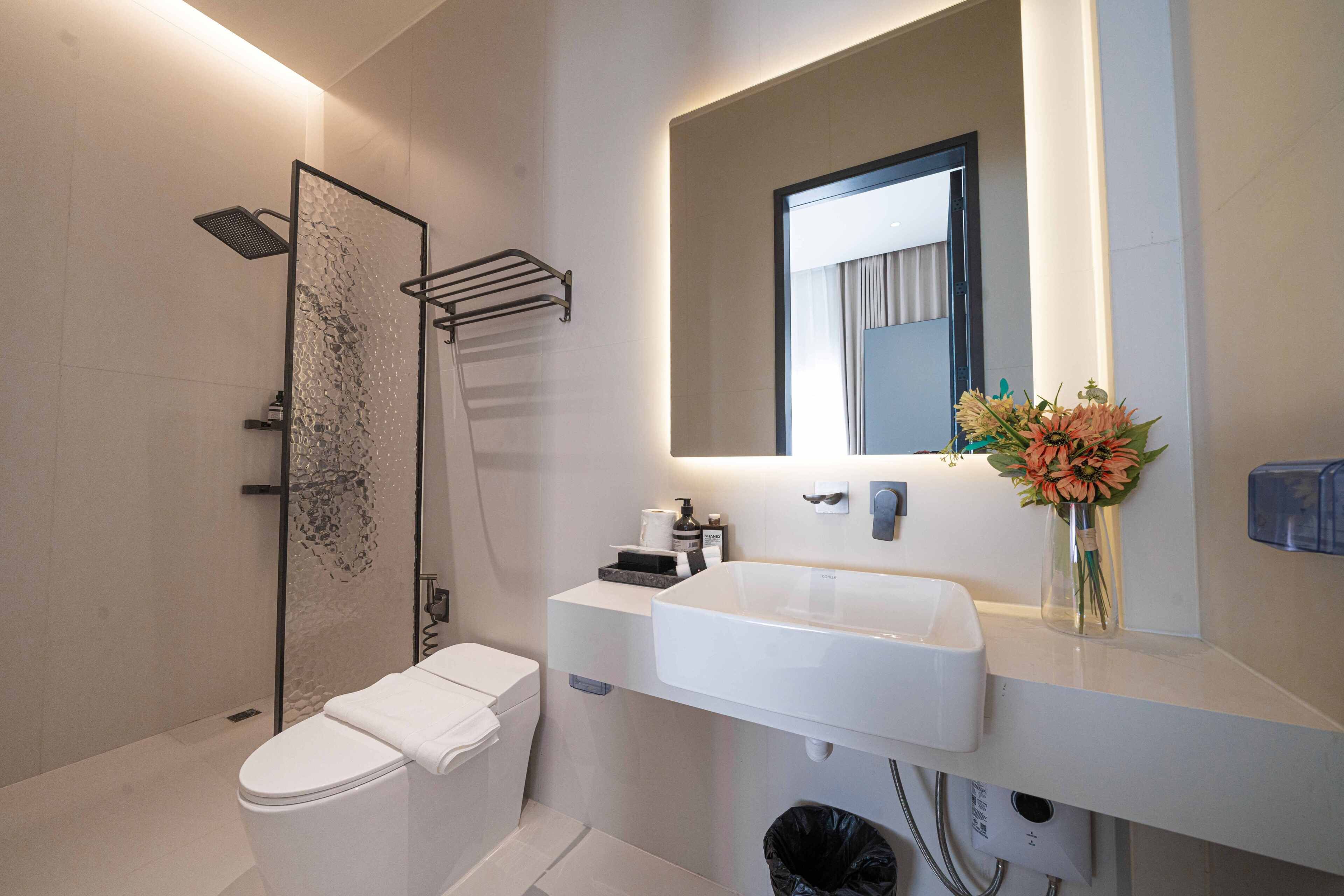 A modern bathroom with a glass shower enclosure, a white toilet, a sink with a mirror above it, and a vase with flowers on the countertop.