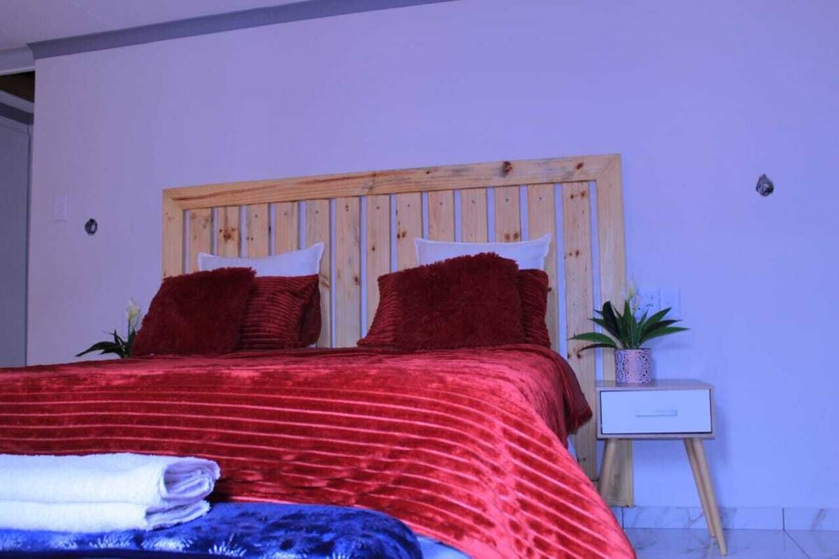 A bed with a wooden headboard, red bedding, and a small bedside table with a plant.