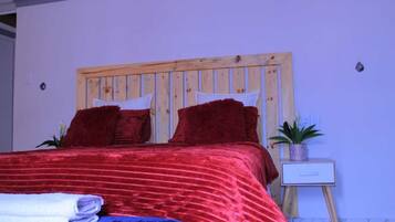 Un lit avec une tête de lit en bois, une literie rouge et une petite table de chevet agrémentée d’une plante.