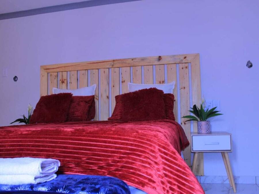 Un lit avec une tête de lit en bois, une literie rouge et une petite table de chevet agrémentée d’une plante.