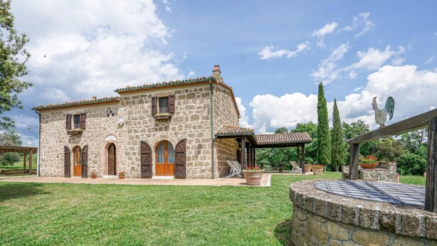 Un bâtiment en pierre avec un toit en tuiles, une porte en bois et un petit jardin agrémenté de plantes en pot.
