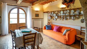Un coin repas accueillant avec une table en bois, des chaises et un canapé orange. On peut voir un porte-ustensiles fixé au mur.