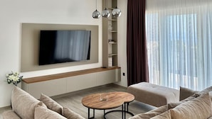 A modern living room with a large flat-screen TV mounted on the wall, a wooden coffee table, and a beige sofa.