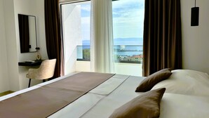 A hotel room with a bed, a desk, a chair, and a view of the sea.