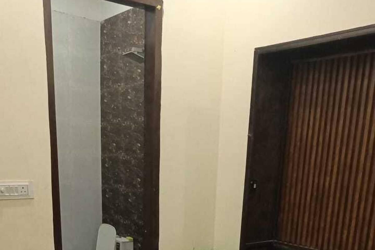 Une chambre à coucher avec un lit, une tête de lit en bois, une poubelle verte et des toilettes visibles à travers une porte ouverte.