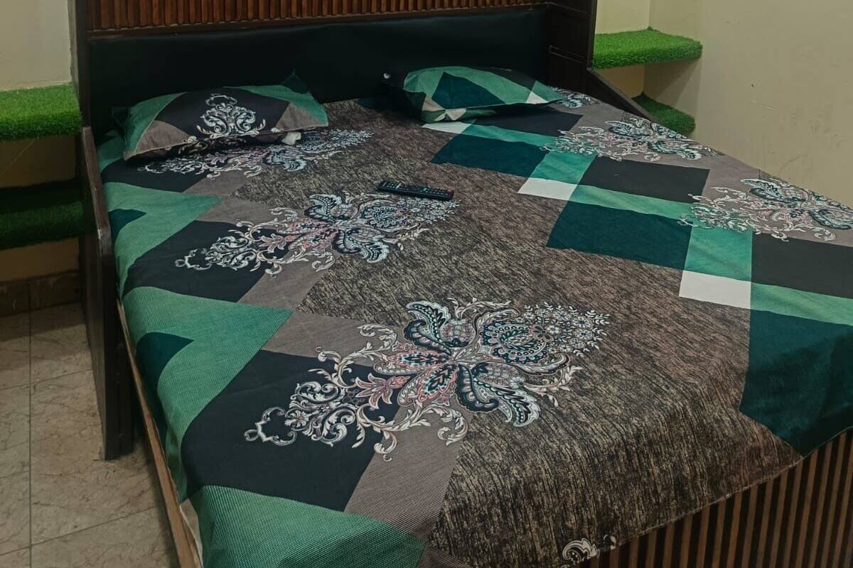 Une chambre avec un lit, une tête de lit en bois, un climatiseur et une petite plante verte sur le rebord de la fenêtre.
