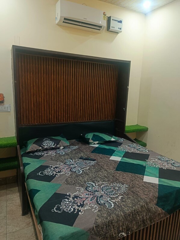A room with a bed, a wooden headboard, an air conditioner, and a small green plant on the windowsill. - Elvin Hotel Karnal (Karnal)