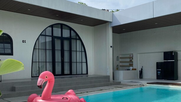 Una casa moderna con piscina, un flotador con forma de flamenco rosa y un amplio ventanal arqueado.