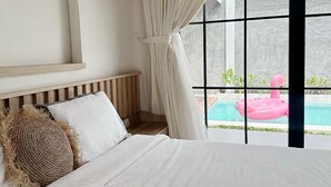 Un dormitorio con una cama grande, cabecero de madera, cojín de tejido y vistas a una piscina con un flotador en forma de flamenco rosa.