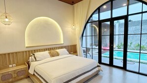 A spacious bedroom with a large bed, a curved window, and a view of a swimming pool. - Pinnara Borobudur  Private 2 BR Villa  (Borobudur)
