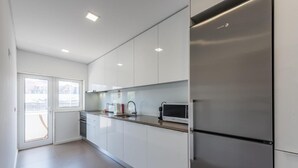 Une cuisine moderne avec des armoires blanches, des appareils en acier inoxydable et une grande fenêtre.