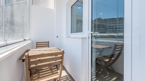 Un balcon avec une table et des chaises en bois, une fenêtre et une vue sur des immeubles.