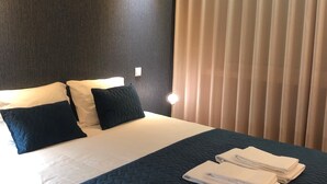 Une chambre d’hôtel avec un lit, des oreillers, une lampe de chevet et une fenêtre avec des rideaux.