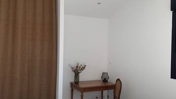 A room with a bed, a wooden table with a chair, a vase with flowers, and a black lamp.