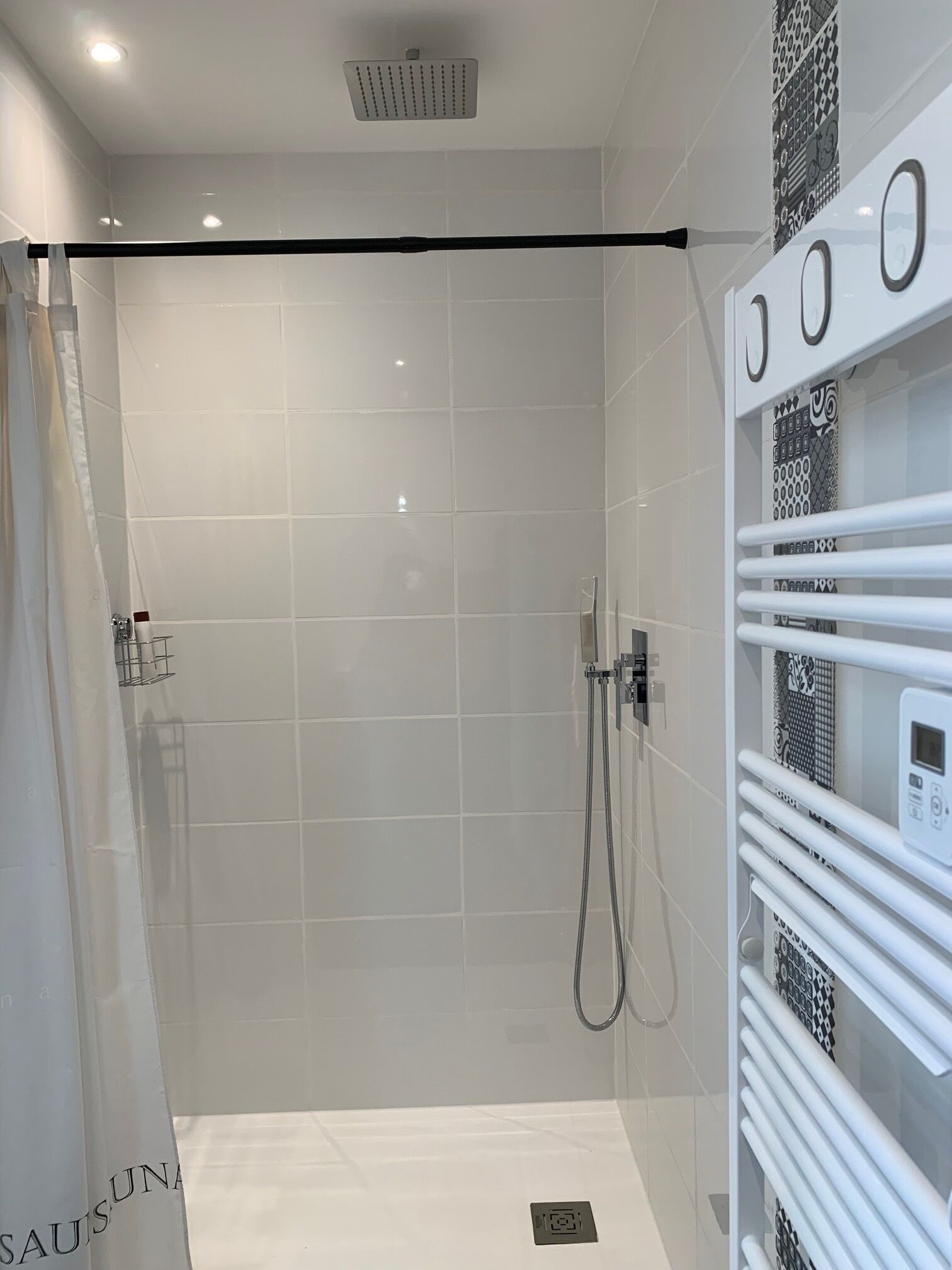A modern bathroom with a glass shower enclosure, white tiled walls, and a built-in towel rack.
