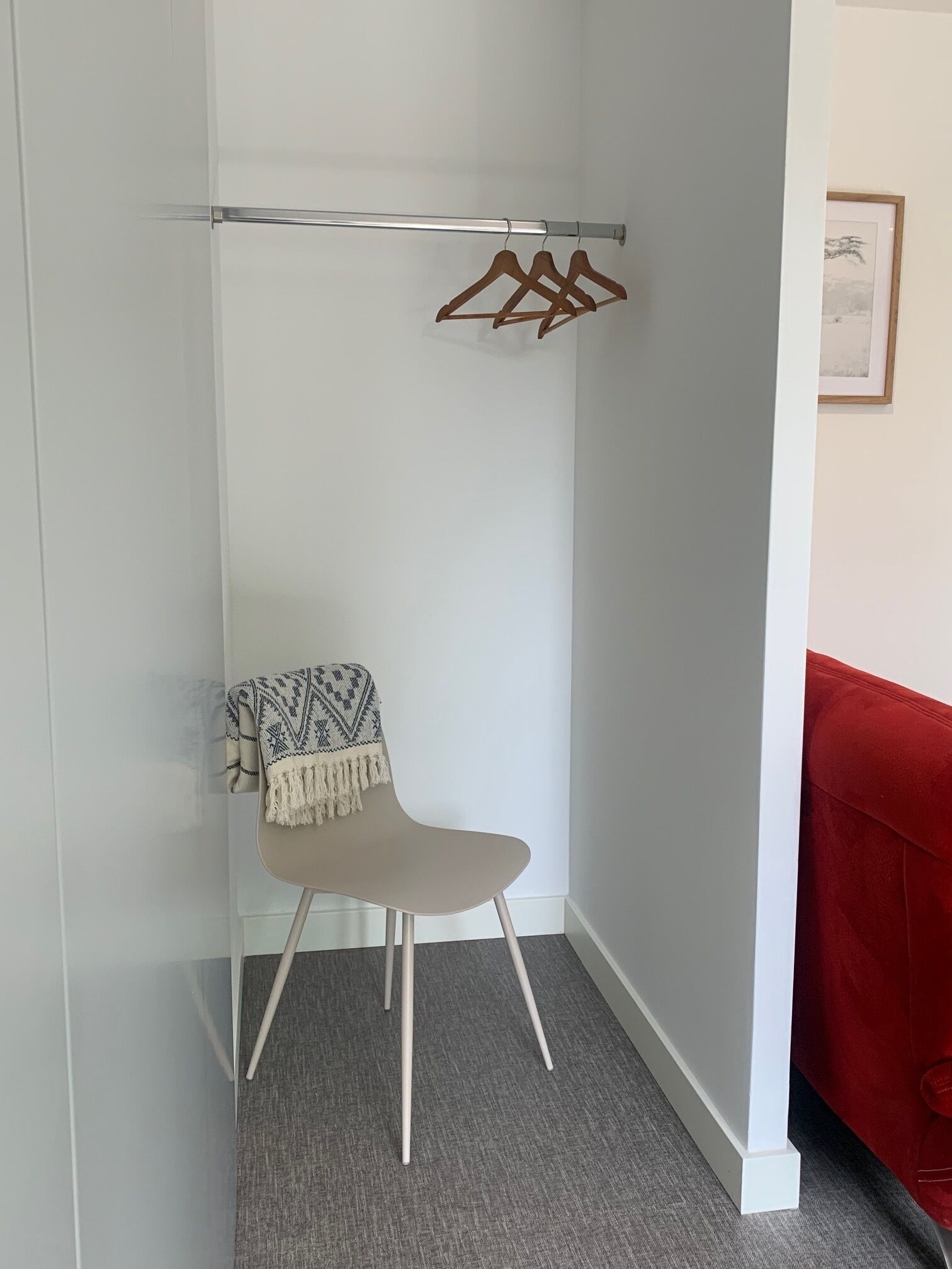 A corner room with a chair, a coat rack, and a red couch.