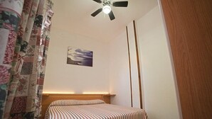 Ein Schlafzimmer mit einem Bett, einem Deckenventilator, einem Nachttisch und einem an der Wand hängenden Bild.