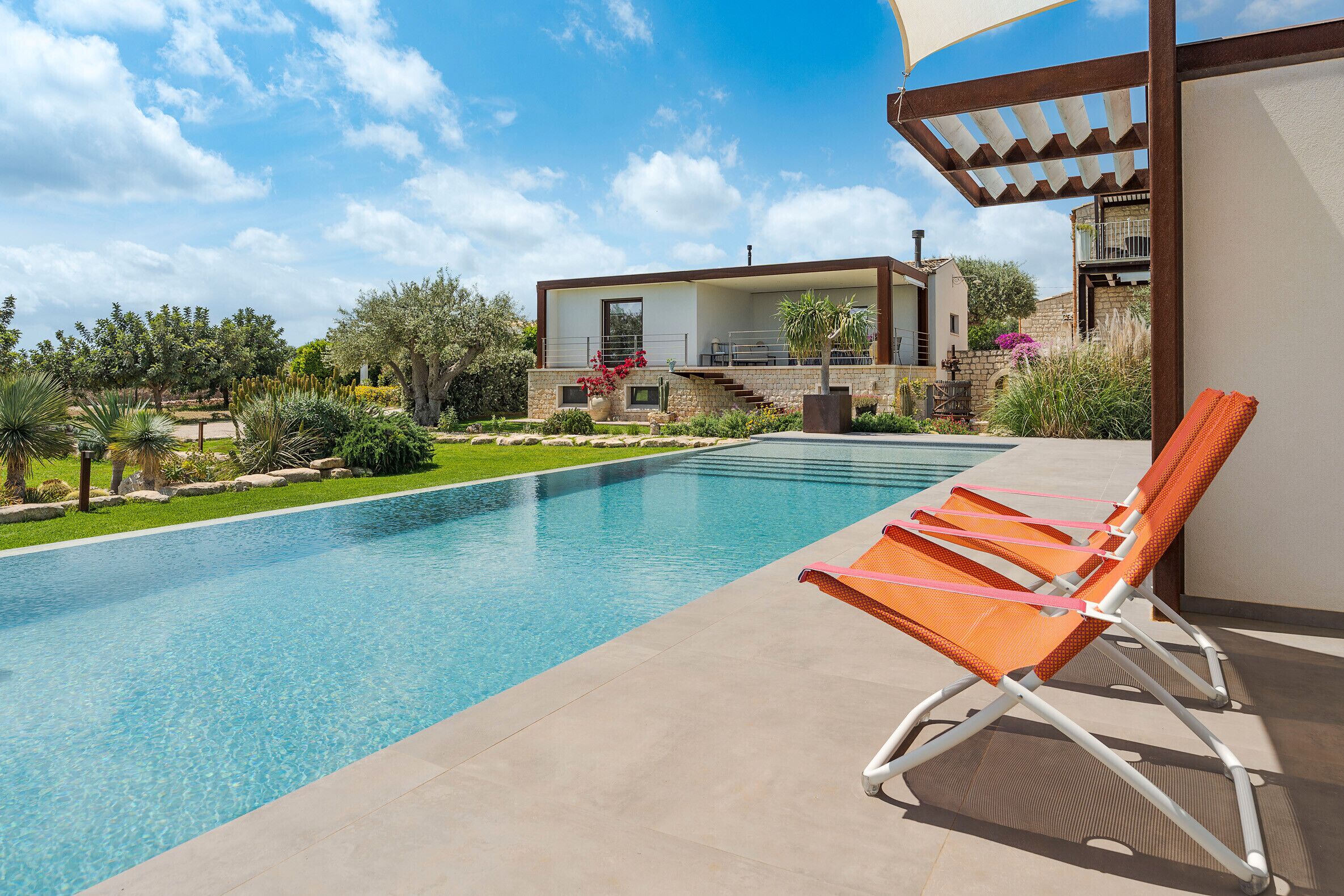 Una casa moderna con piscina, mobiliario de exterior y jardín.
