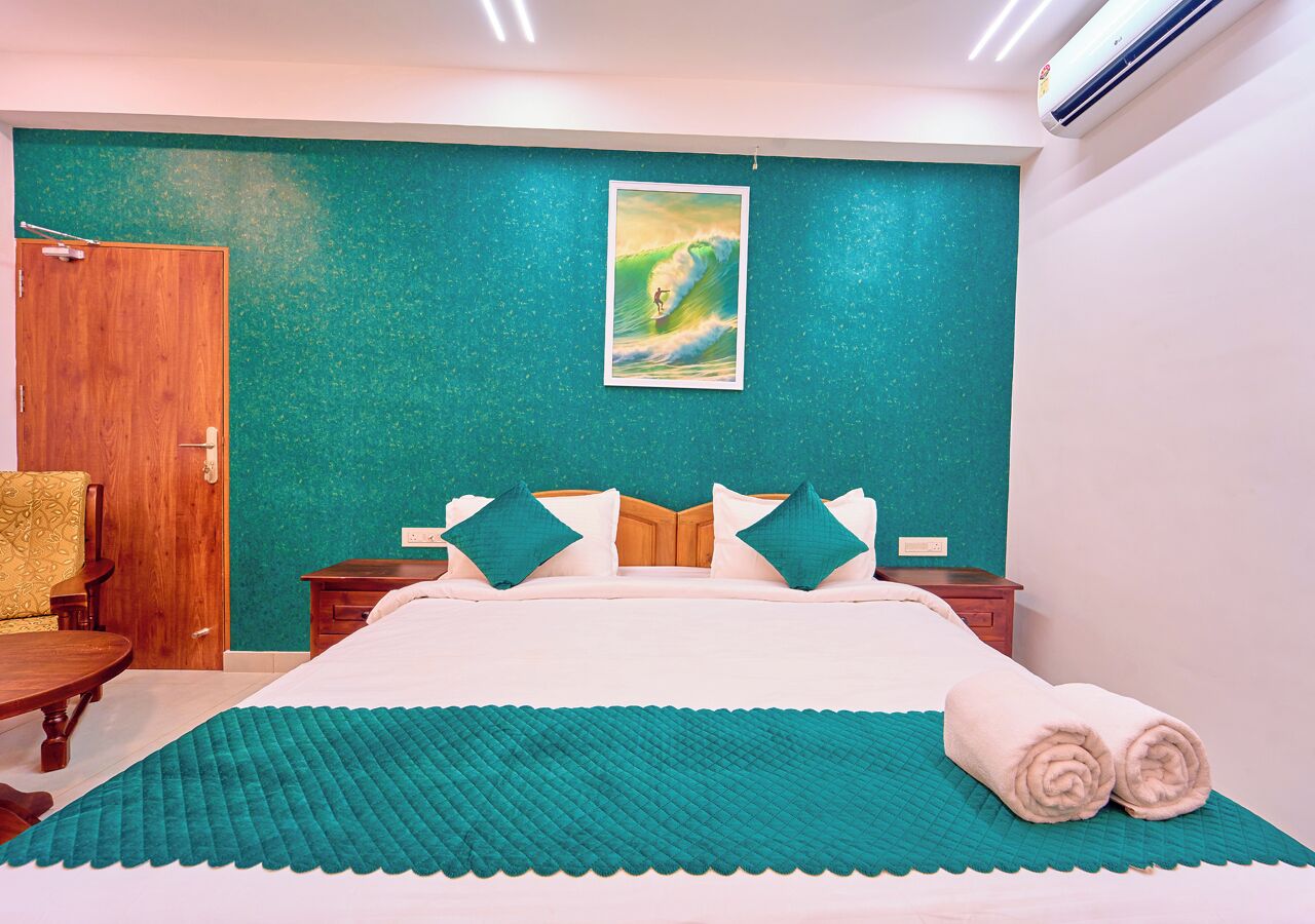 A hotel room with a bed, a painting of a surfer, and a teal-colored wall.