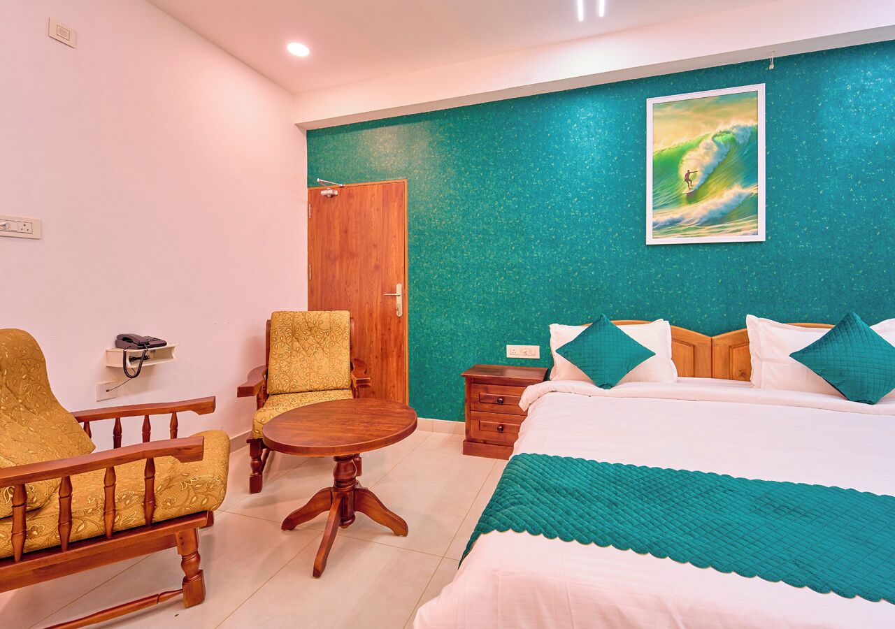 A hotel room with a bed, two armchairs, a wooden table, and a green accent wall.