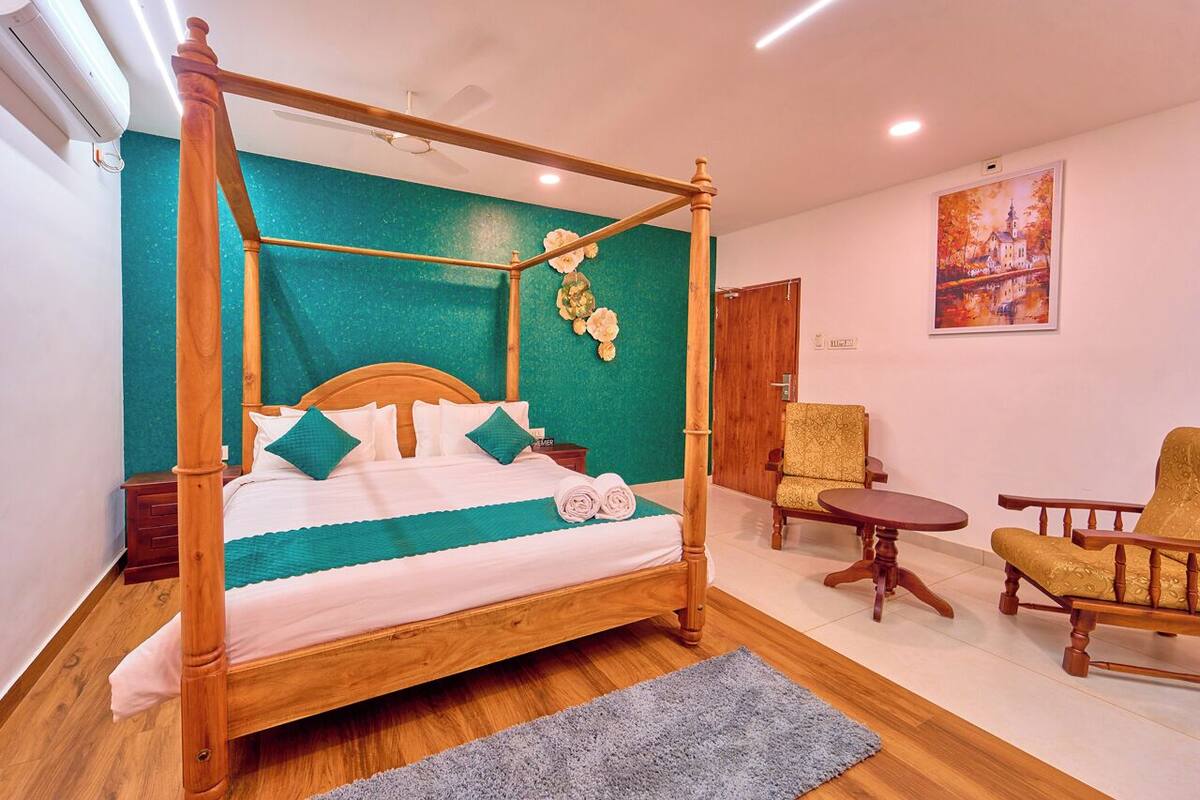 A four-poster bed with a teal accent wall, a small round table, and two chairs.
