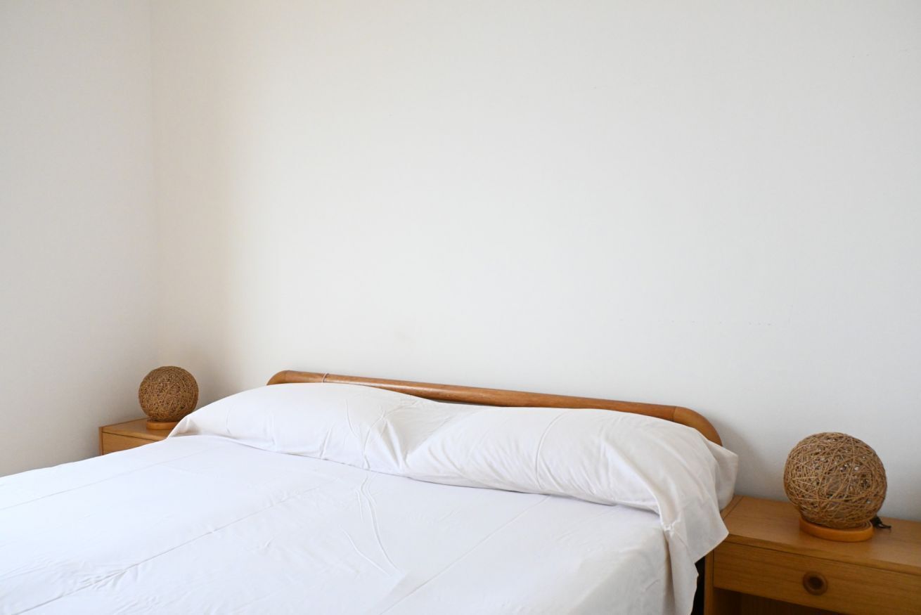A bed with white linens, a wooden headboard, and two nightstands with woven decorative items.