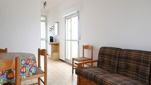 A room with a wooden dining table, a plaid sofa, a wooden chair, a small cabinet, and a window with blinds. - SE164 - Marotta, Three-Room Apartment with Sea View and Terrace (Marotta)