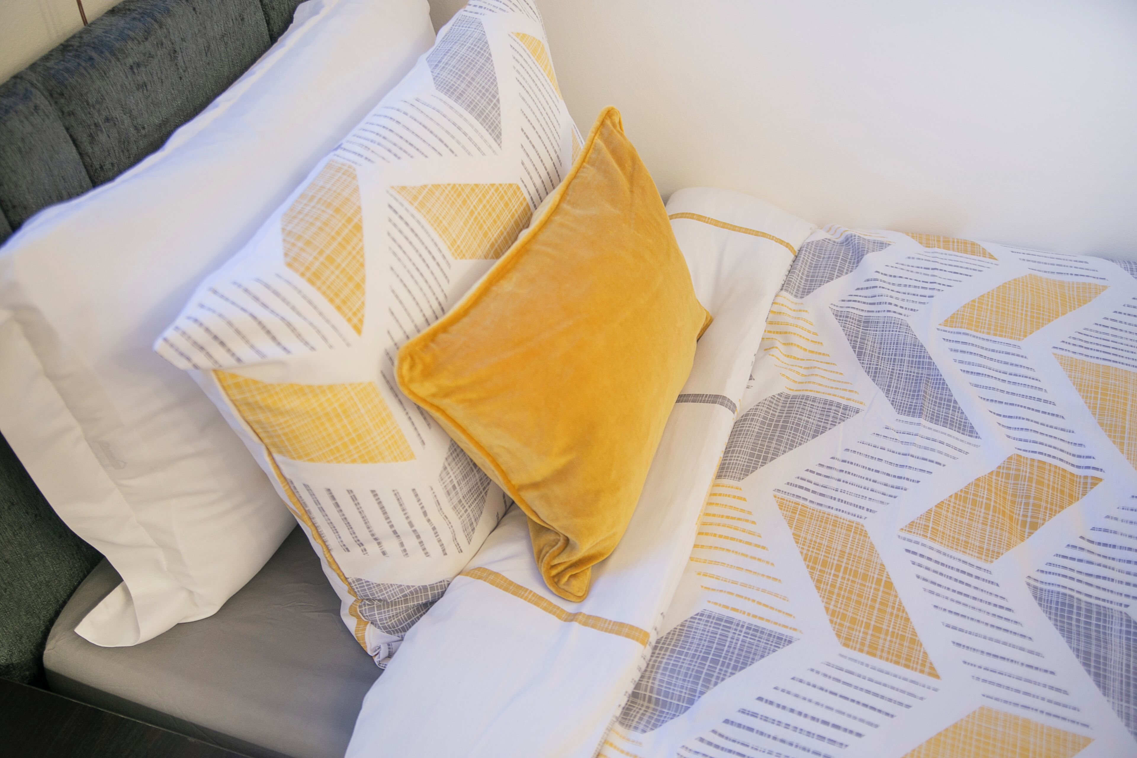 Un lit avec une couvre-lit à motifs et des oreillers, une tête de lit grise et un mur blanc.