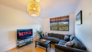 Ett modernt vardagsrum med en stor platt-TV, en soffa, ett soffbord och en hängande lampa.